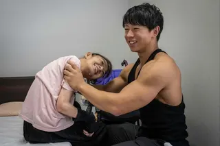 Care worker and bodybuilder Takuya Usui (right) chats with Madoka Yamaguchi as he helps her sit on a bed at a care home for people with disabilities operated by Visionary in Ichinomiya, Aichi prefecture. Photo: AFP