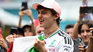 Kimi Antonelli celebrates his race win in Miami while holding the Italian flag. A crowd are gathered around him and taking photographs