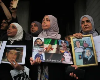 Women wearing headscarves hold up photographs of relatives