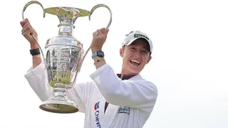 Nelly Korda is wearing a white dressing gown and baseball cap and holding the Chevron Championship in the air