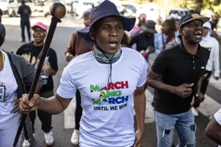 AFP via Getty Images A man wearing a white T-shirt with the slogan: March and March until we win over a South African flag, and holding a stick, on an anti-migrant march