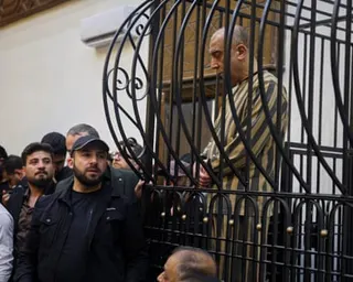 Atef Najib sits in the defendants’ cage as a crowd of people look on