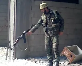 A man in combat uniform points an automatic rifle towards the ground