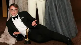 A man in a tuxedo lies on the floor in front of a golden Oscar statuette