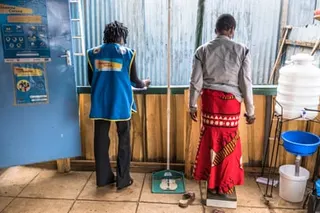 An African woman stands on scales beside another woman