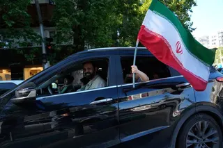 A child holds an Iranian flag through the window of a vehicle in northern Tehran, Iran