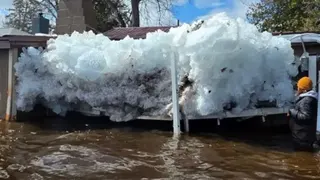 A giant chunk of ice before a home. A man stands nearby for scale.