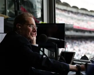 a man sits in a broadcasting booth at a baseball stadium