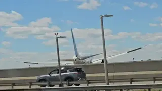 A plane flying over a bridge which a car is driving on. The plane is just past the the bridge and it is very low in the air