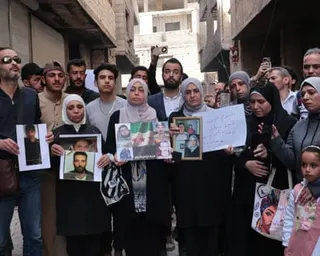 A large group of people hold up photos of relatives