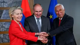 A woman in a red jacket puts her hands on top of the hands of two men both in blue suits