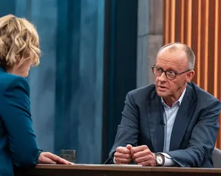 Friedrich Merz speaking to Caren Miosga across a TV studio interview table