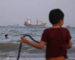 Children play in the water along the shore bulk carriers, cargo ships, and service vessels sit offshore in the strait of Hormuz, off Bandar Abbas, Iran.