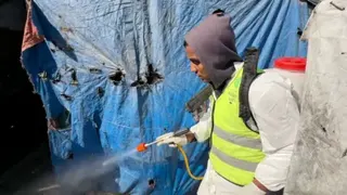 A member of pest control, wears white clothing and sprays into the makeshift homes