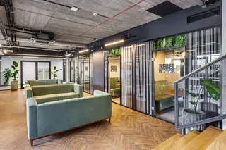 Green sofas and glass walls in the inside of a modern-looking office. It's Rebel Wolves' office in Poland, the developer of The Blood of Dawnwalker.