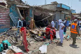 Plainclothes police officers, left, and local residents examine damage at the site of a bomb explosion at a market.
