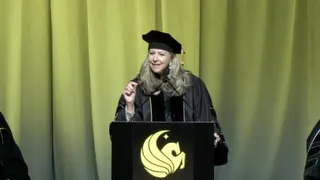 a woman in graduation robes speaks into a microphone