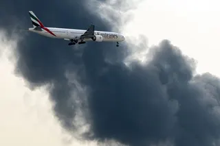 An Emirates Boeing 777 aircraft prepares for landing as a smoke plume rises from an ongoing fire at Dubai International Airport