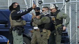 CORRECTION / Immigration and Customs Enforcement (ICE) agents use their phones near protestors at a demonstration in Newark, New Jersey May 7, 2025, outside Delaney Hall, a newly converted immigrant detention centre. Delaney Hall has the ability to hold over a 1000 people, and the detention facility, privately owned by The GEO Group, holds a contract with the federal government to house people arrested by ICE. (Photo by TIMOTHY A. CLARY / AFP) / "The erroneous mention[s] appearing in the me