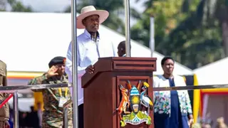 Government of Uganda/X President Yoweri Museveni, in a white shirt and a white hat, stands before a lectern withe the Ugandan coat of arms