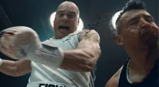 heavyset bald man in a boxing ring, spattered with blood, preparing to rain down a heavy blow on his cowering opponent