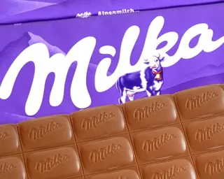A Milka chocolate bar sits in front of purple packaging featuring the Milka logo and cow