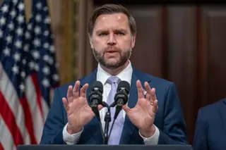 JD Vance gestures with both hands while speaking at microphones, with an American flag behind him.