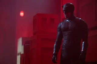 man in daredevil suit standing on a rooftop bathed in red light