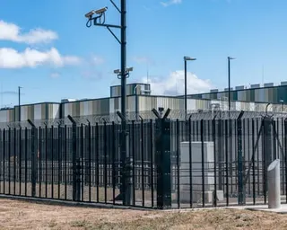 A high security fence with razor wire and surveillance cameras surrounds a data centre facility.