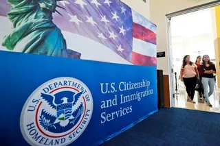 Three people walking through a doorway next to a blue U.S. Citizenship and Immigration Services sign with a Department of Homeland Security seal on it.