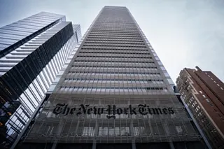 The New York Times Building, a tall modern skyscraper, rises above adjacent buildings, viewed from street level