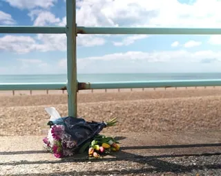 A bouquet of flowers is left on a pavement, with Brighton beach and the sea in the background