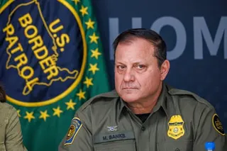 Man in uniform sitting with yellow badge and flag behind him