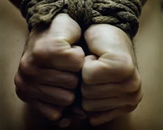 Two clenched fists bound together with frayed rope against a blurred background