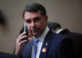 Senator Flavio Bolsonaro in a dark suit holds a phone to his ear while wearing lapel pins