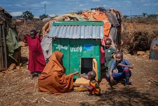 一名索马里妇女和儿童在索马里巴伊多阿（Baidoa）巴瓦科（Barwaaqo）难民营的一个干旱的国内流离失所者安置点内，于一个绿色的联合国儿童基金会鸡舍旁摆姿势。