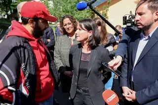 Getty Images Local mayor Johanna Rolland (C), wearing a black jacket, top and trousers, speaks to a man wearing a red cap and hoodie and a dark jacket. A microphone is held above her head and several other journalists are seen recording her remarks with phones and microphones.