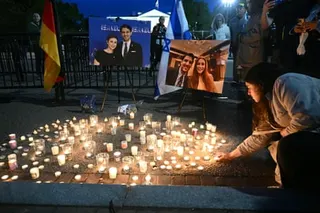 A person kneels to light candles arranged on the ground in front of photographs displayed on easels