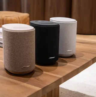 Three Bose Ultra Speakers on a wooden coffee table in beige, black, and white.