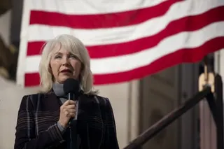 Woman speaks into microphone in front of flag