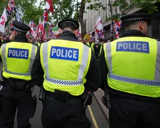 Three police officers in high-visibility vests stand in a line facing a crowd with flags