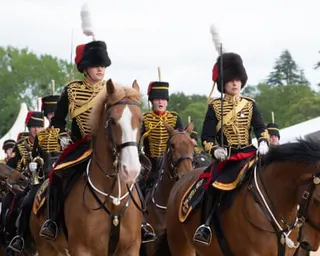 King's Troop soldiers in black and gold ceremonial uniforms with tall fur hats ride horses