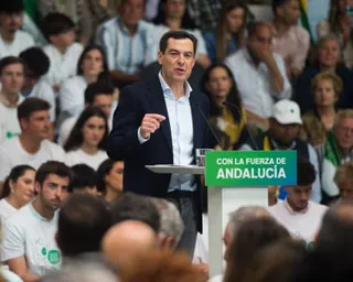 Moreno Bonilla speaks at podium bearing the words 'Con la fuerza de Andalucía' in the middle of an audience wearing white and green T-shirts