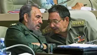 AFP via Getty Images Fidel Castro and his brother Raul are seen seated wearing military uniforms. Fidel is speaking and Raul is leaning in to hear him.