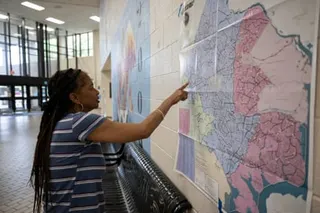 A woman points to a congressional district map posted on a wall in a hallway