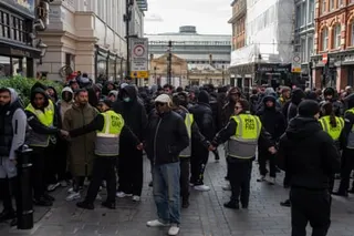 A line of security people in hi-vis vests linking arms to keep a crowd back
