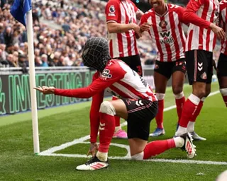 Enzo Le Fée wears a Spiderman mask and crouches in the superhero's pose by the corner flag