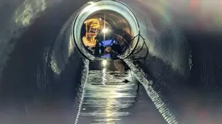 一台自主偵測機器人位於一根長長的污水管的一端，水流沿著管道底部流動。