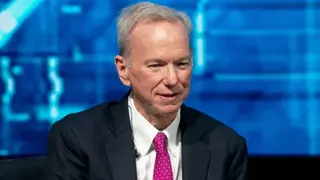 Getty Images Eric Schmidt sits with his hands crossed and looks ahead. He is wearing a black suit, a white shirt, and a hot pink polka-dot tie. In the background is a blue screen that features different shades of blue.