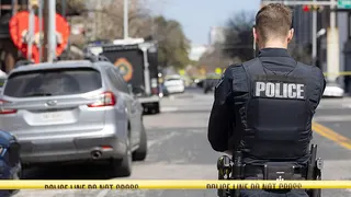 A police officer stands near crime scene tape blocking a city street.
